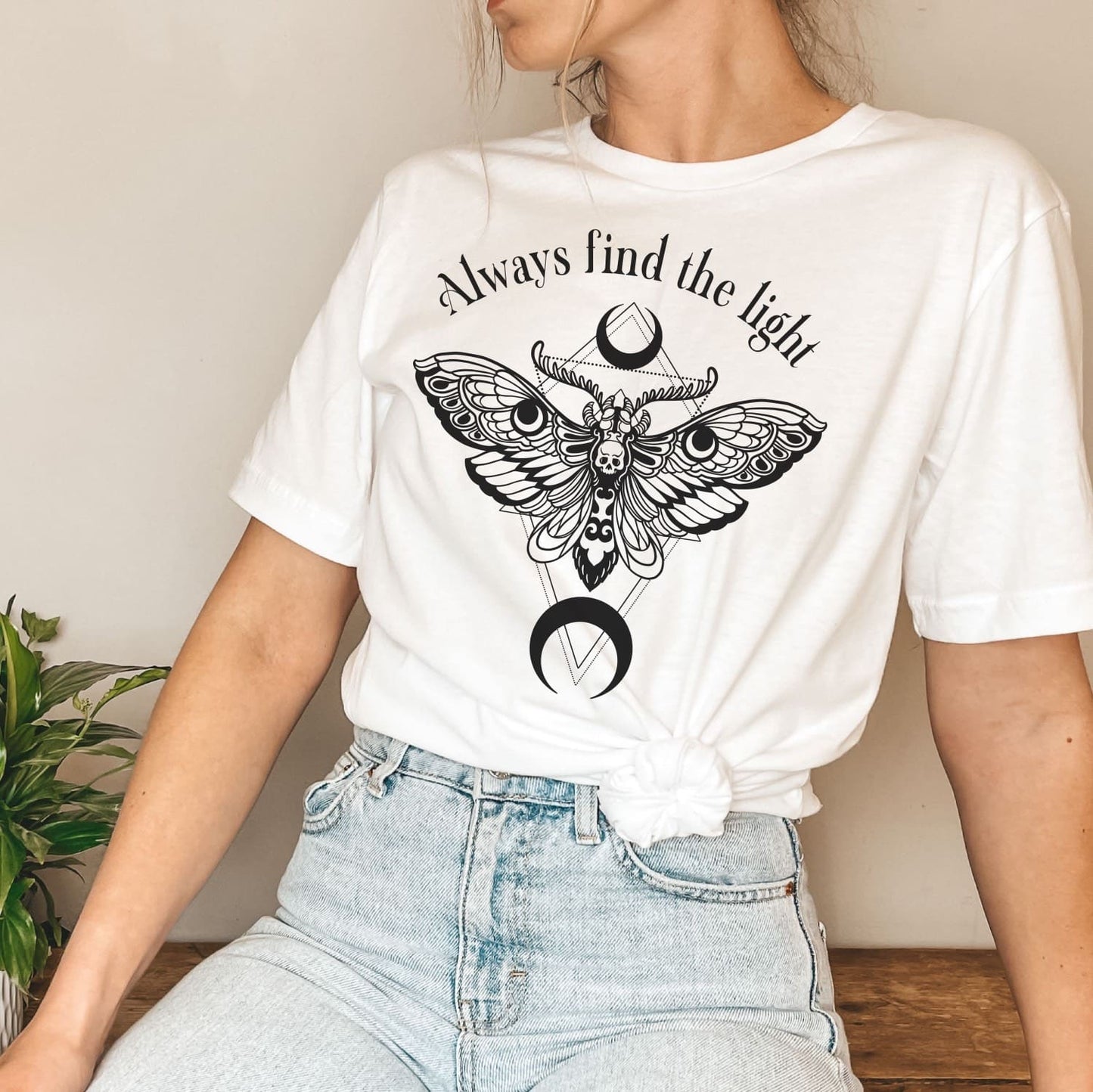 Person wearing a white inspirational t-shirt with a moth design and 'Always find the light' text.