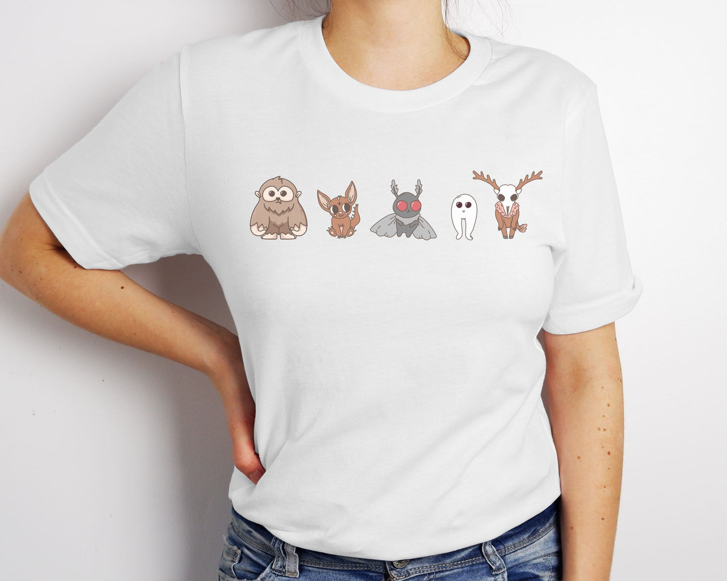 White t-shirt with cartoon character designs on a plain background: Cute Cryptids Comfort Colors Shirt, Kawaii Bigfoot Chupacabra Mothman Fresno Wendigo Tee, Funny Cryptidcore Gift, Folklore Mythology T-Shirt