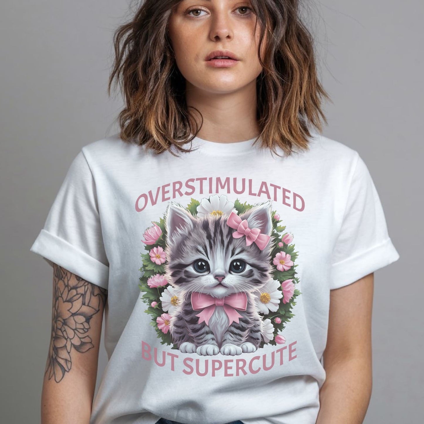Person wearing a white t-shirt with a kitten graphic and text: Overstimulated Shirt, Neurodiversity Tee, ADHD Burnout Tshirt, Autism Awareness, Gift For Neurospicy Autistic, Cute Pink Bow Cat T-Shirt