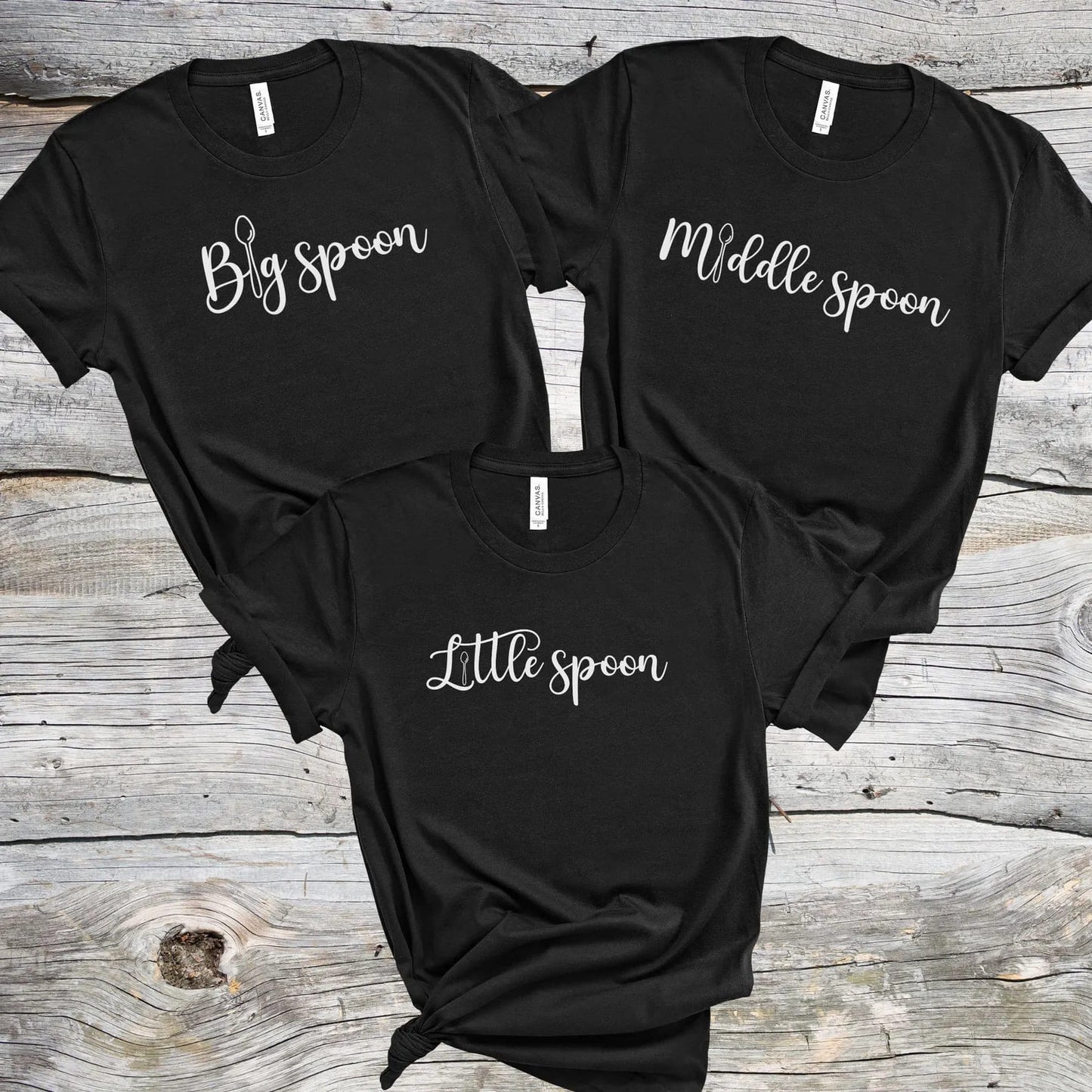 Three matching ENM polyamory black t-shirts with 'Big spoon', 'Middle spoon', and 'Little spoon' text on a wooden surface.