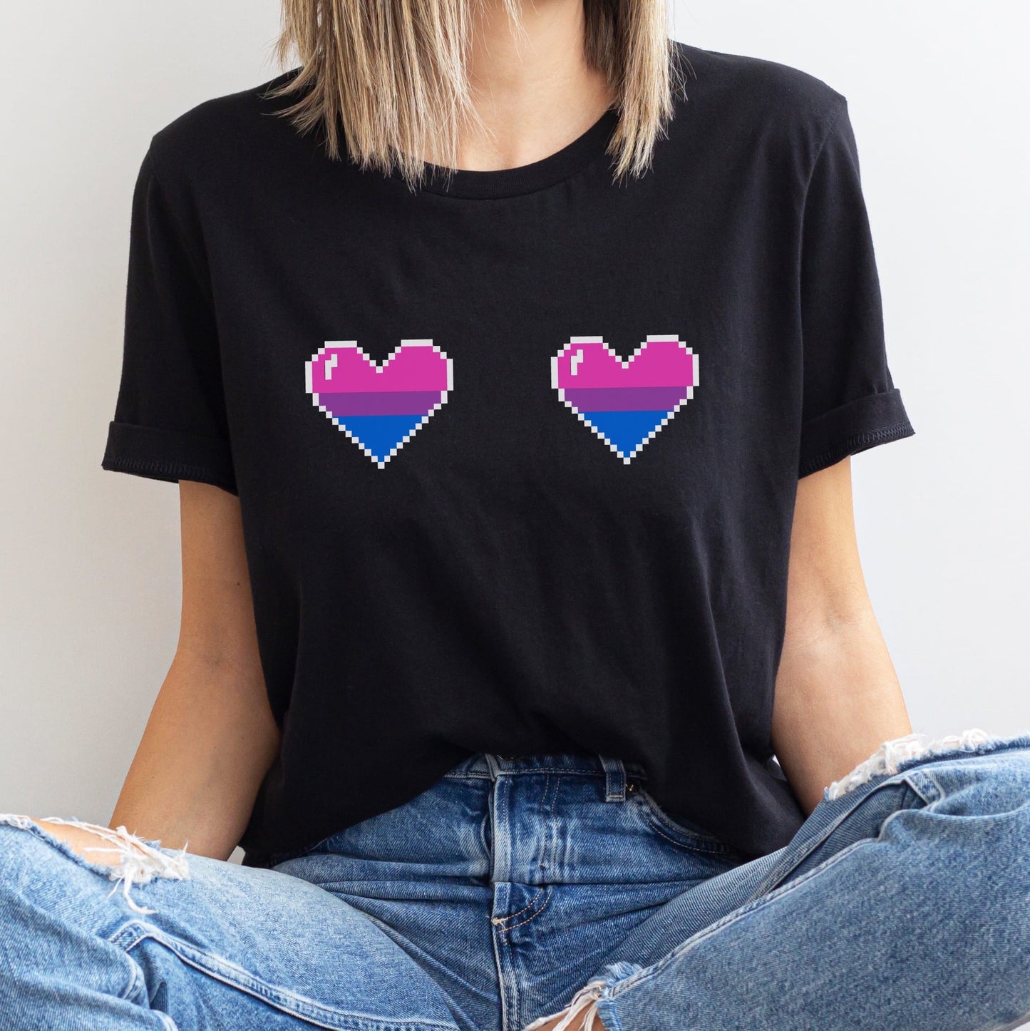 Person wearing a black t-shirt with pixelated bisexual pride hearts design.