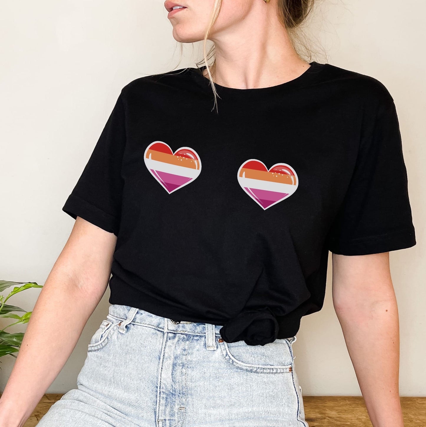 WLW Person wearing a black t-shirt with lesbian sunset flag heart designs on a plain background