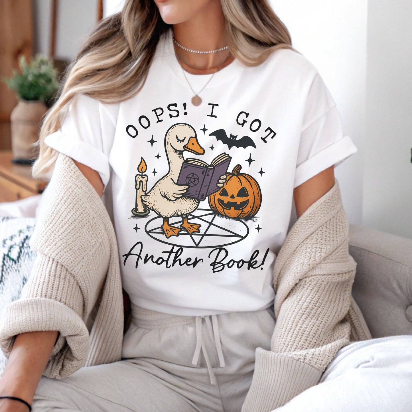 Person wearing a white t-shirt with a graphic design and text, sitting on a couch: Funny Bookish Goose Shirt, Spooky Season Book Tee, Fall Library T-Shirt, Reading Gift For Halloween Lover Cute Trick Or Treat Teacher Outfit