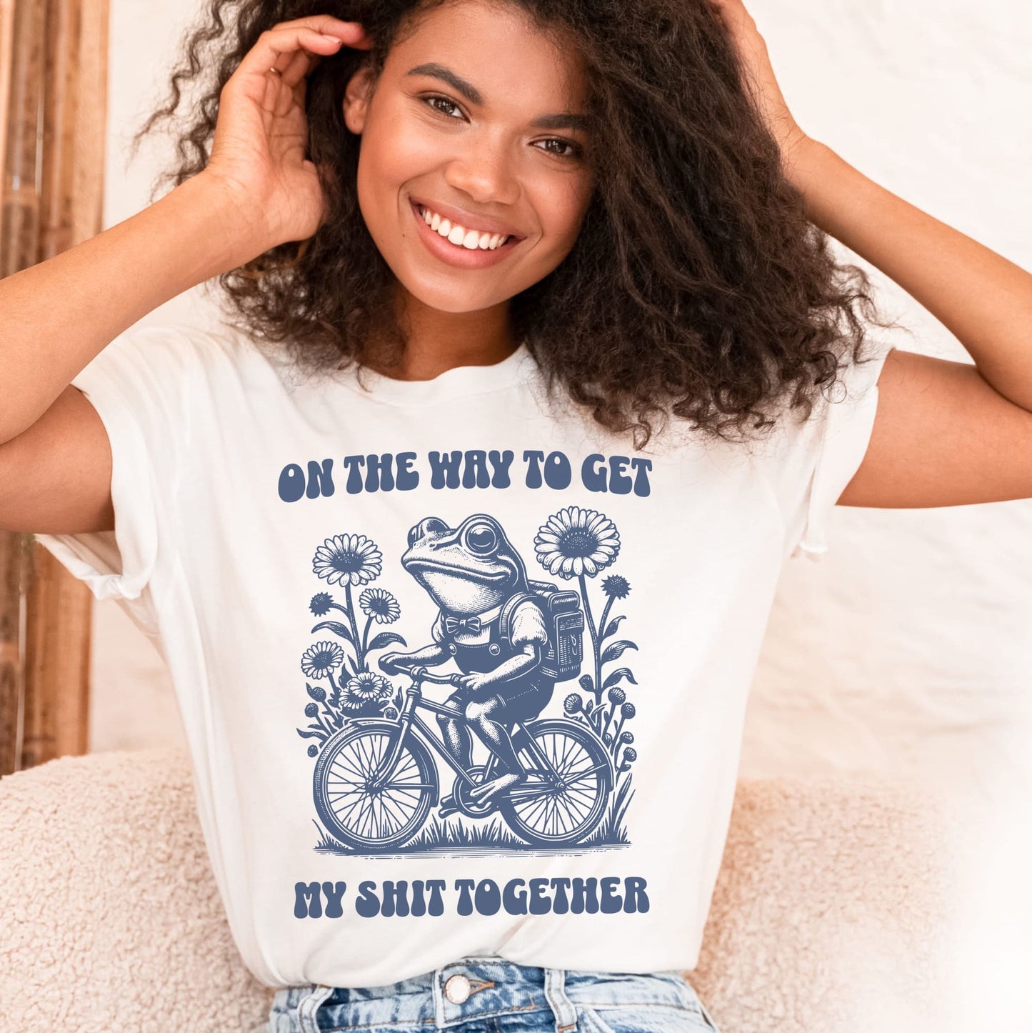 Woman wearing a white t-shirt with a graphic design and text, sitting on a couch: Funny Neurodivergent Shirt, ADHD AuDHD Tee, Mental Health T-Shirt, Vintage Frog, Sarcastic Adult Humor, On The Way To Get My Shit Together