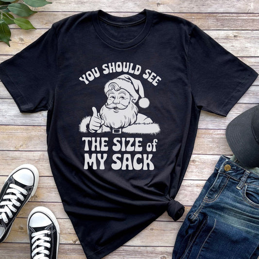 Black t-shirt with Santa Claus graphic and text on a wooden surface with shoes and jeans: Rude Santa Men's T-Shirt, Funny Adult Humor Christmas Tee, Holiday Season Gift, Boyfriend Shirt, Spicy Husband Present, Gift For Him