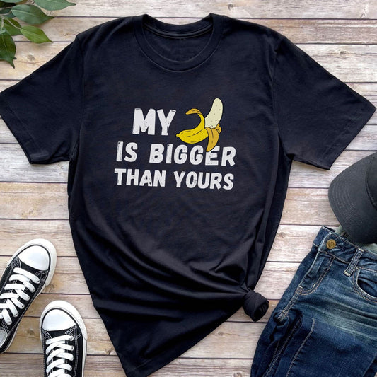 Black t-shirt with banana graphic and text on a wooden surface with shoes and jeans.