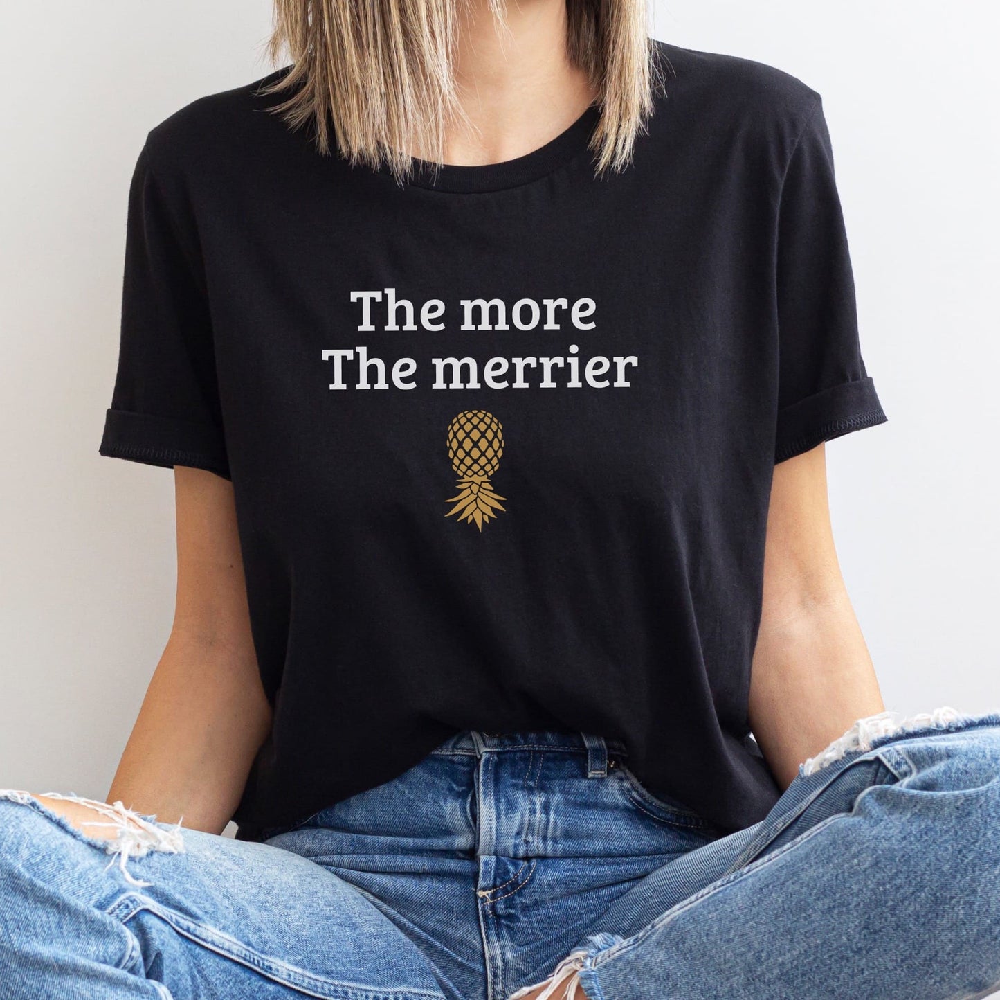 Person wearing a black t-shirt with 'The more The merrier' text and pineapple graphic: Funny Swingers Shirt, Upside Down Pineapple Tee, Subtle Adult Humor T-Shirt, Fun Hotwife Tshirt, Gift For Swinging Non Monogamy Couples