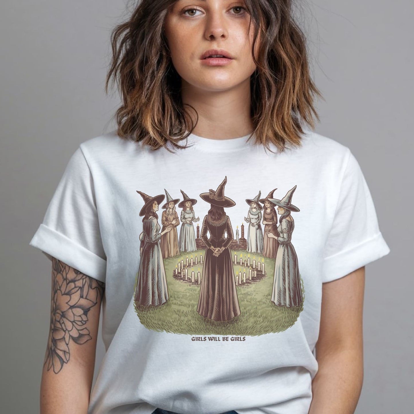 Person wearing a white t-shirt with a graphic design of women in witch costumes.
