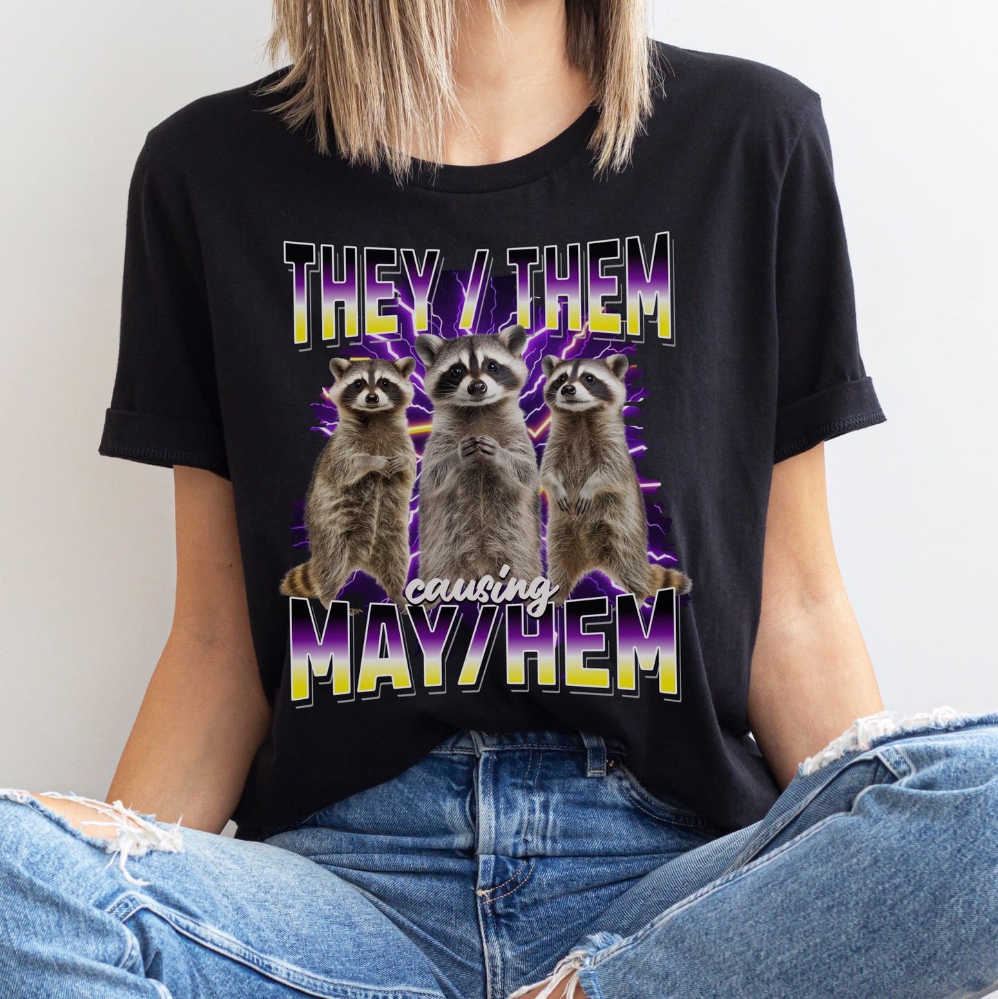Person wearing a black bootleg nonbinary t-shirt with raccoon graphics and they them pronouns.