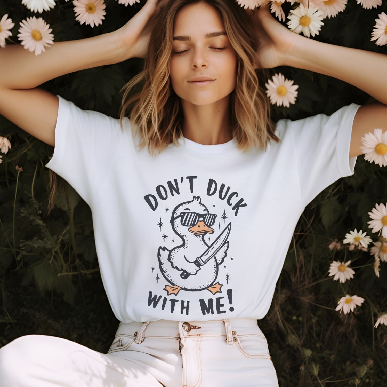 Woman wearing a white t-shirt with a duck graphic and text, lying on the ground with flowers around.