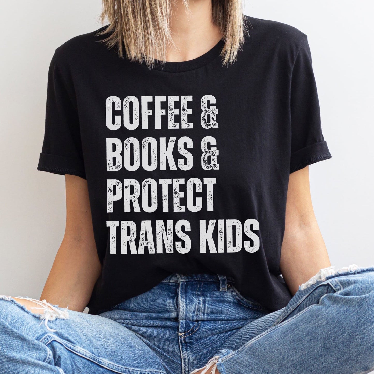 Person wearing a black t-shirt with 'COFFEE & BOOKS & PROTECT TRANS KIDS' text.