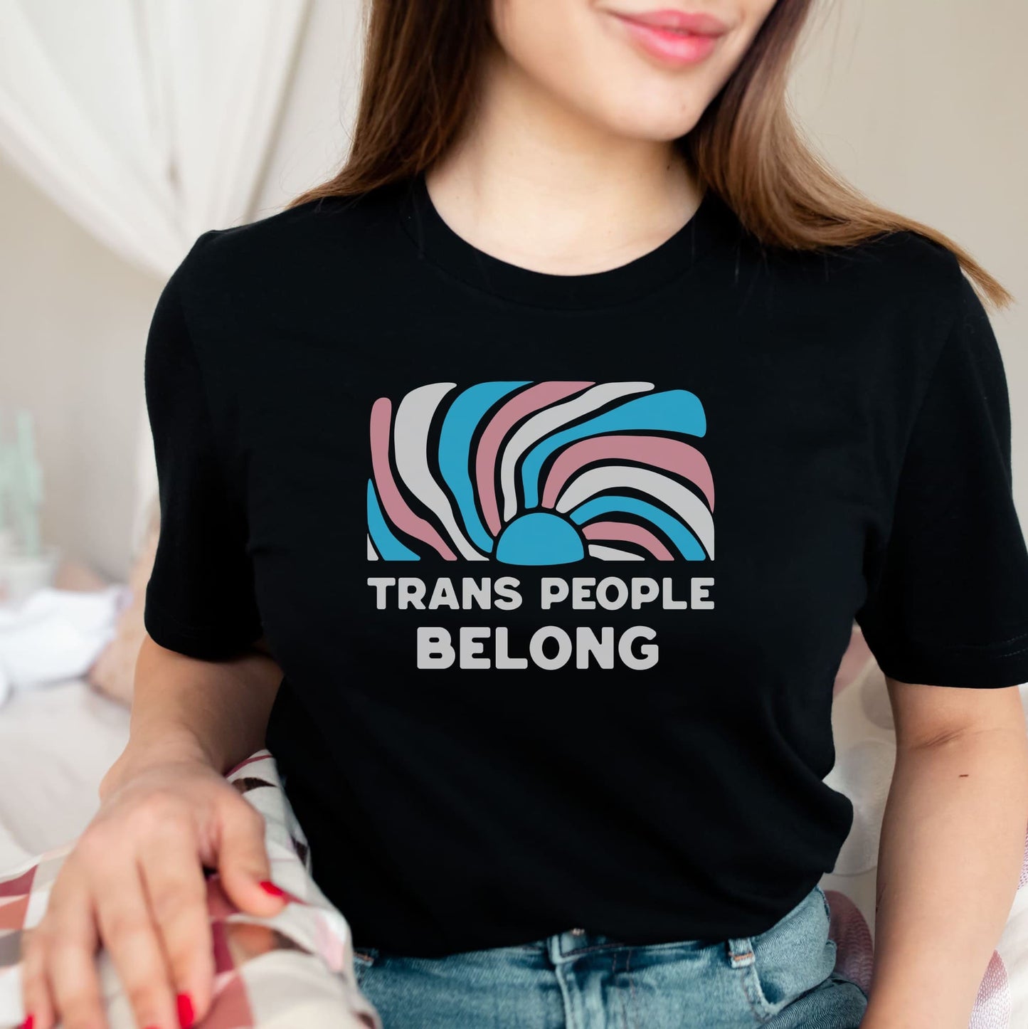 Person wearing a black t-shirt with 'Trans People Belong' text and abstract design.