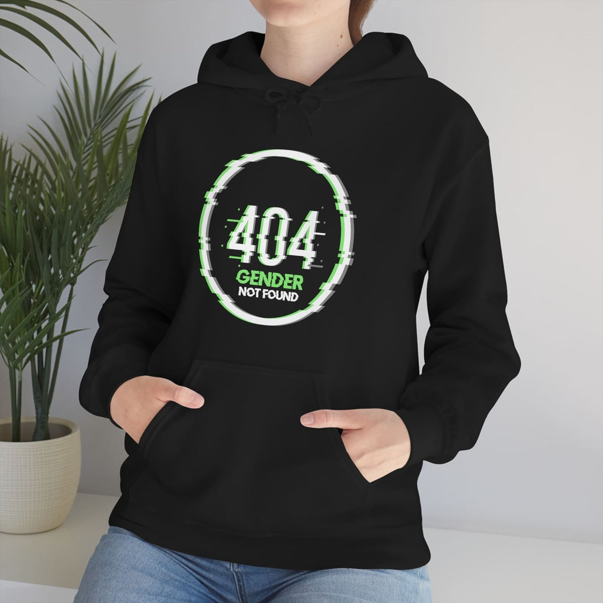 Person wearing a black agender  hoodie with '404 Gender Not Found' design, standing indoors with a plant in the background.