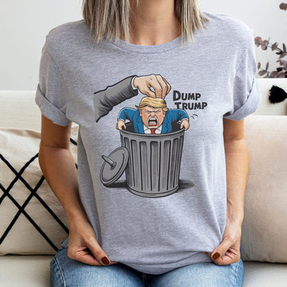 Person wearing a gray t-shirt with a graphic of a hand dumping a figure labeled 'Dump Trump' into a trash bin: Anti Trump shirt, Anti Trumpism shirt, Dump Donald Trump US election 2024 tshirt, Pro Kamala Harris Walz tee,  Funny political apparel