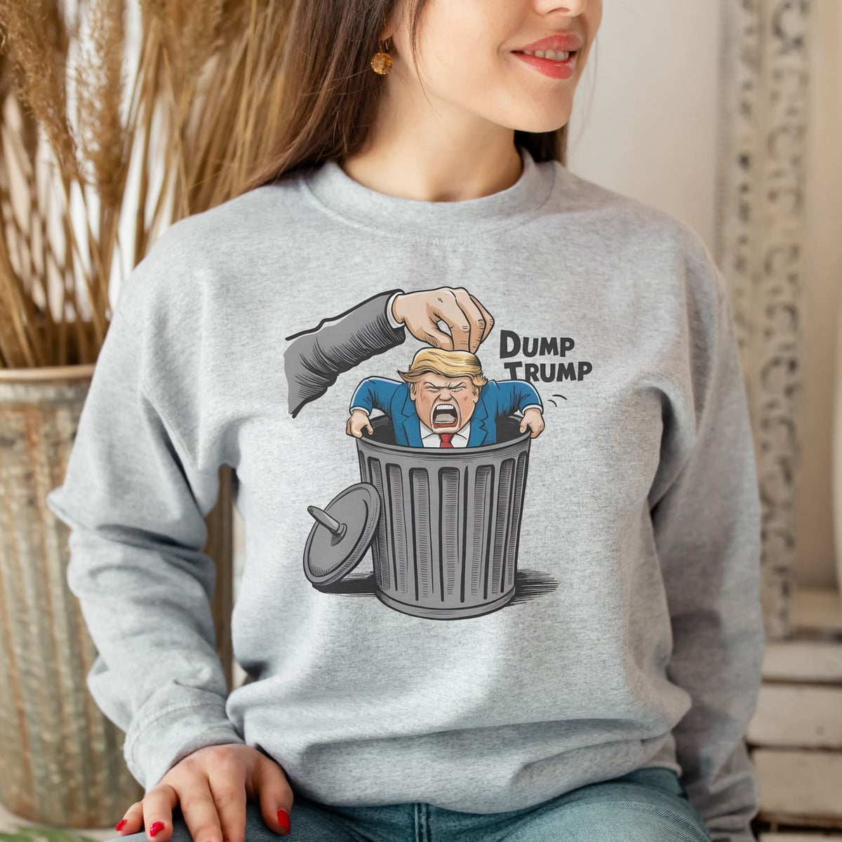 Person wearing a gray sweatshirt with a graphic of a hand dumping a figure labeled 'Dump Trump' into a trash can.
