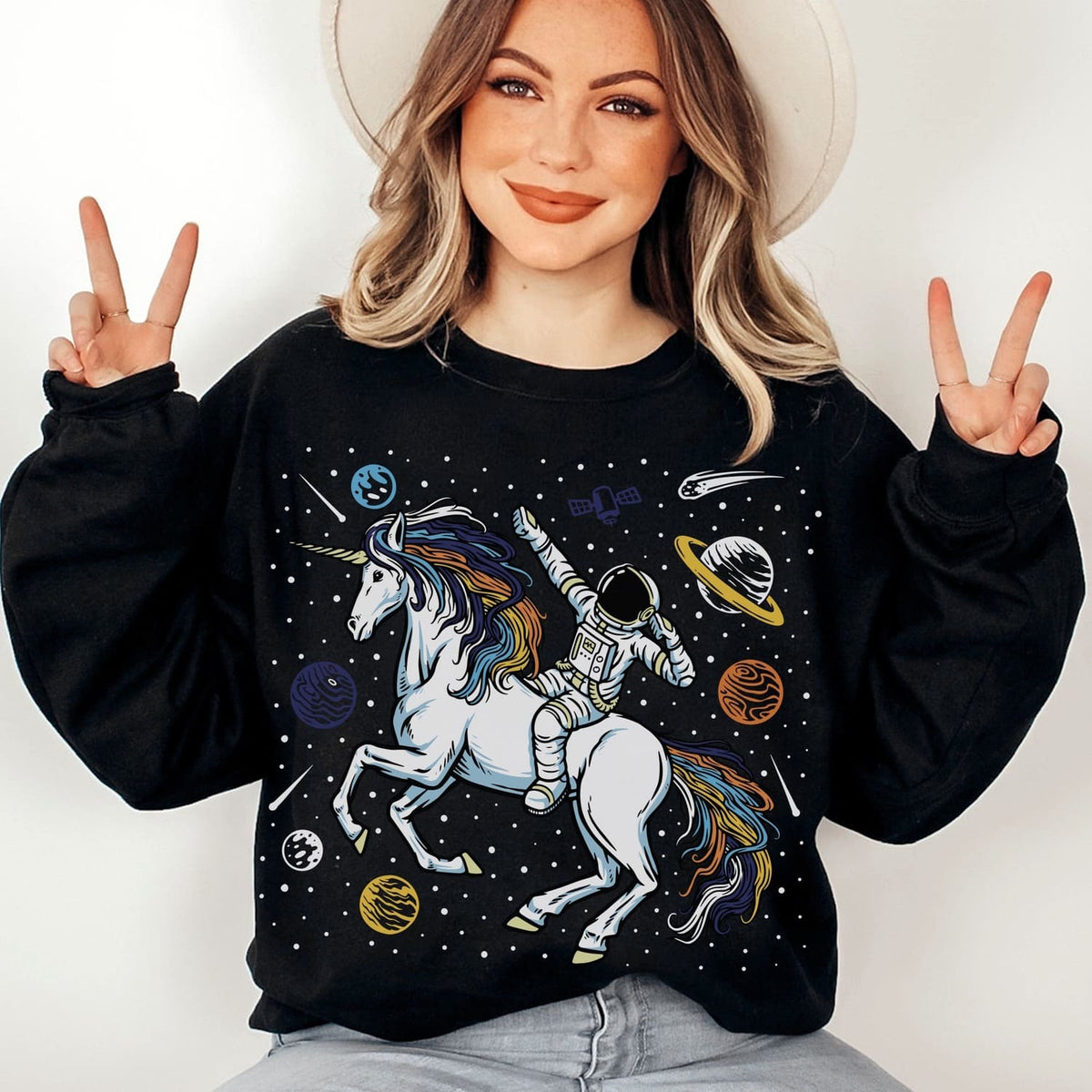 Person wearing a black aroace sweatshirt with a unicorn and astronaut design, making peace signs.