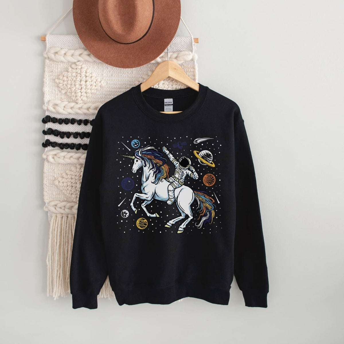 Black sweatshirt with aroace unicorn design on a hanger against a white wall.