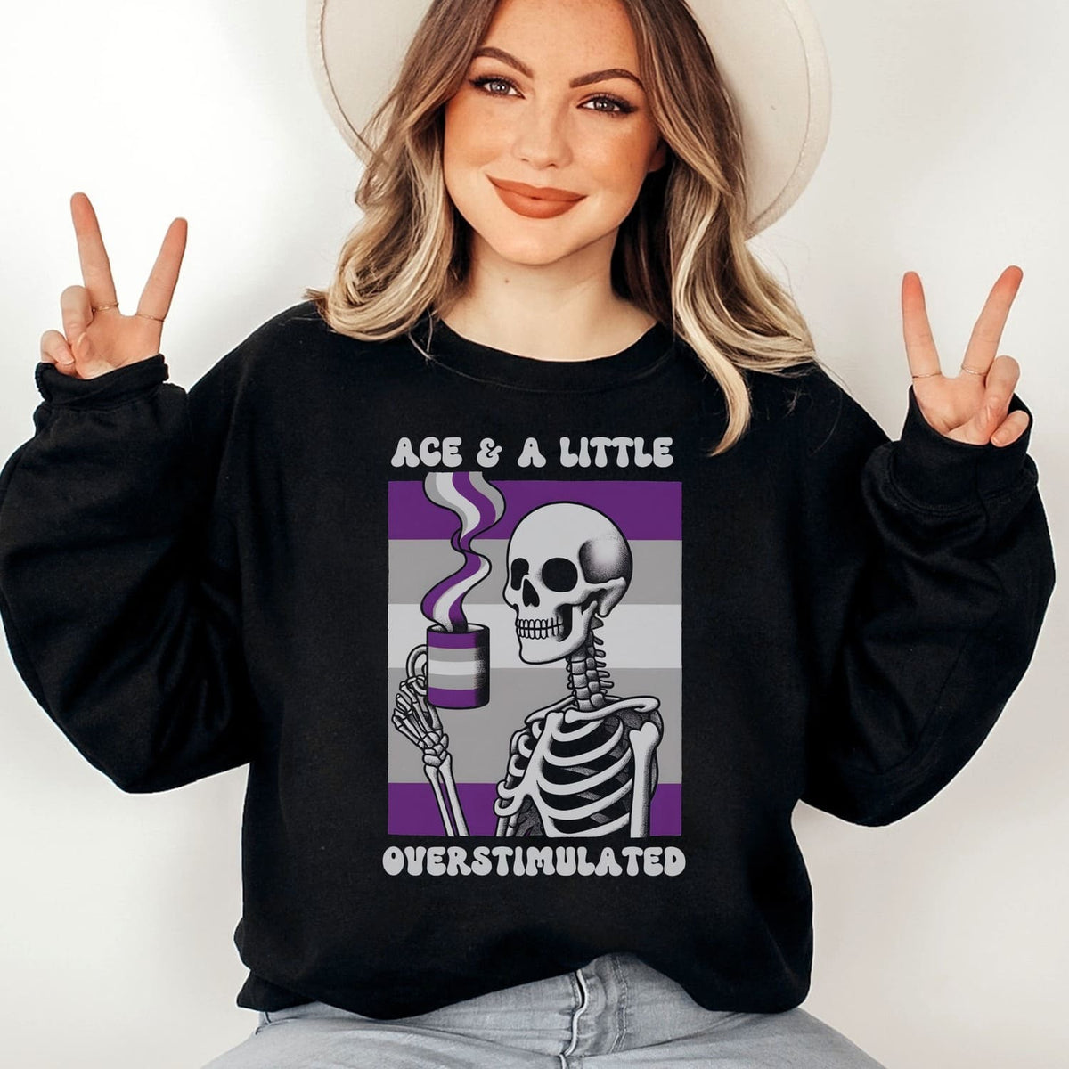 Person wearing a black asexual sweatshirt with a skeleton and coffee cup design, making peace signs.
