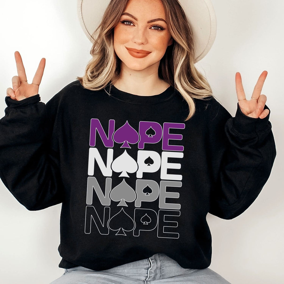 Person wearing a black asexual ace of spades sweatshirt with 'NOPE' text and peace signs.