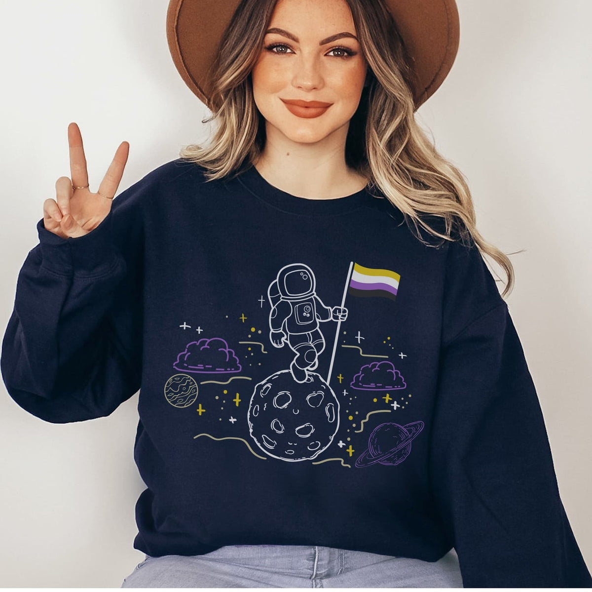 Person wearing a navy blue sweatshirt with a nonbinary astronaut design on a plain background