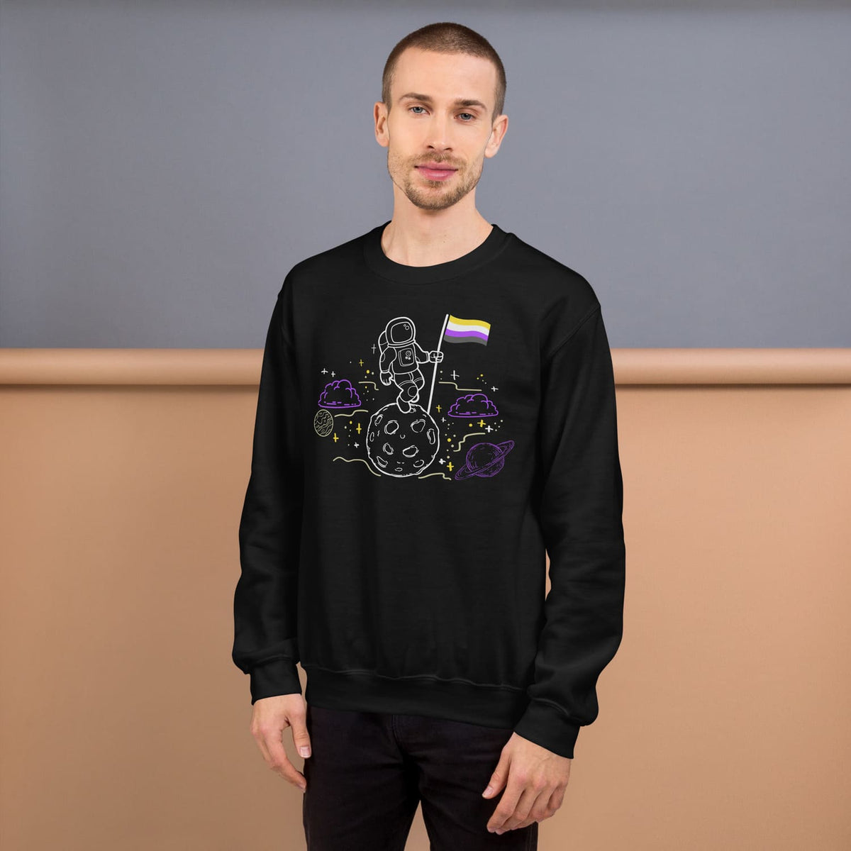 Person wearing a black enby sweatshirt with a space-themed design on a brown and gray background