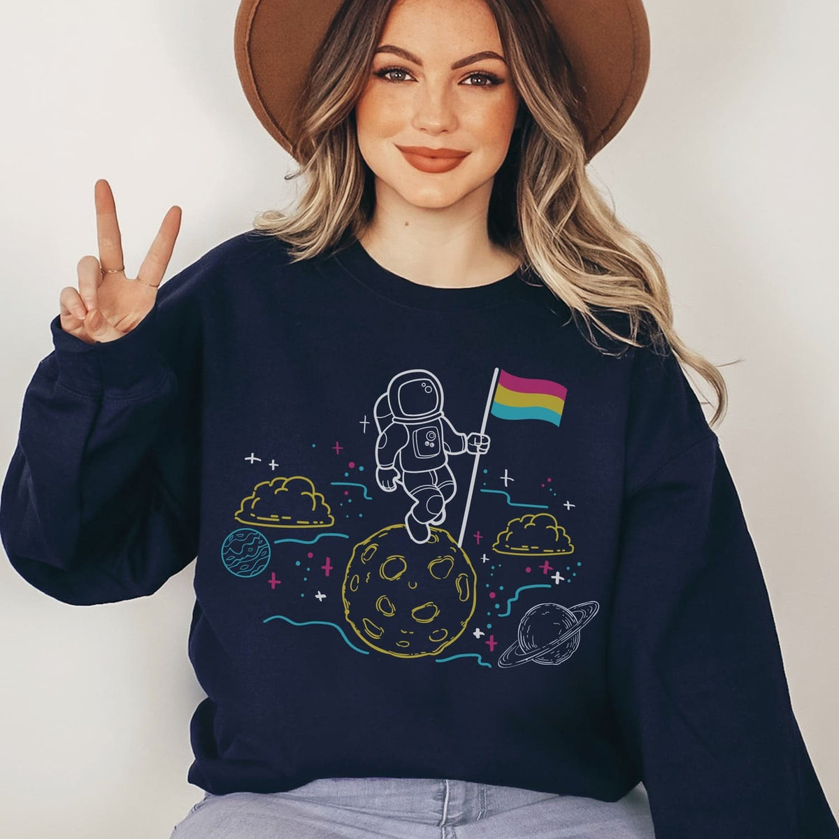 Person wearing a navy blue sweatshirt with a pansexual  astronaut design on a plain background