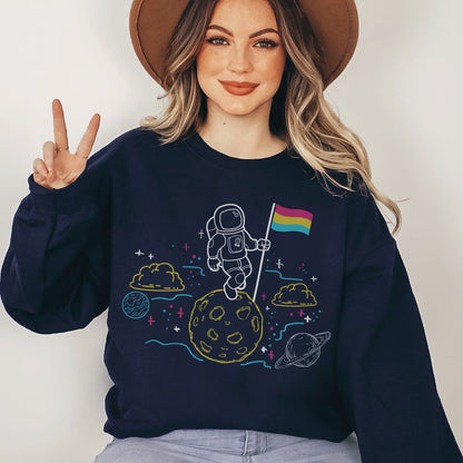 Person wearing a navy blue sweatshirt with a pansexual  astronaut design on a plain background