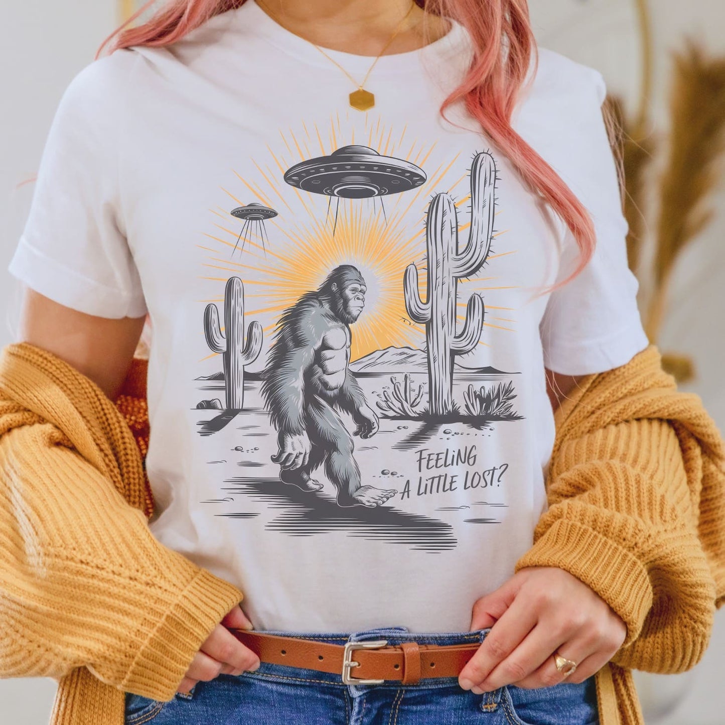 Person wearing a t-shirt with a graphic of a Sasquatch, UFO, and cactus with text 'Feeling a Little Lost?'.