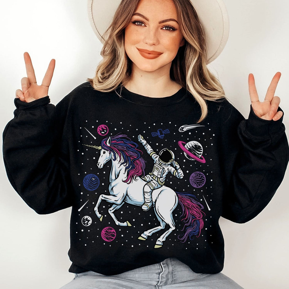 Person wearing a black sweatshirt with a bisexual unicorn and astronaut design, making peace signs.