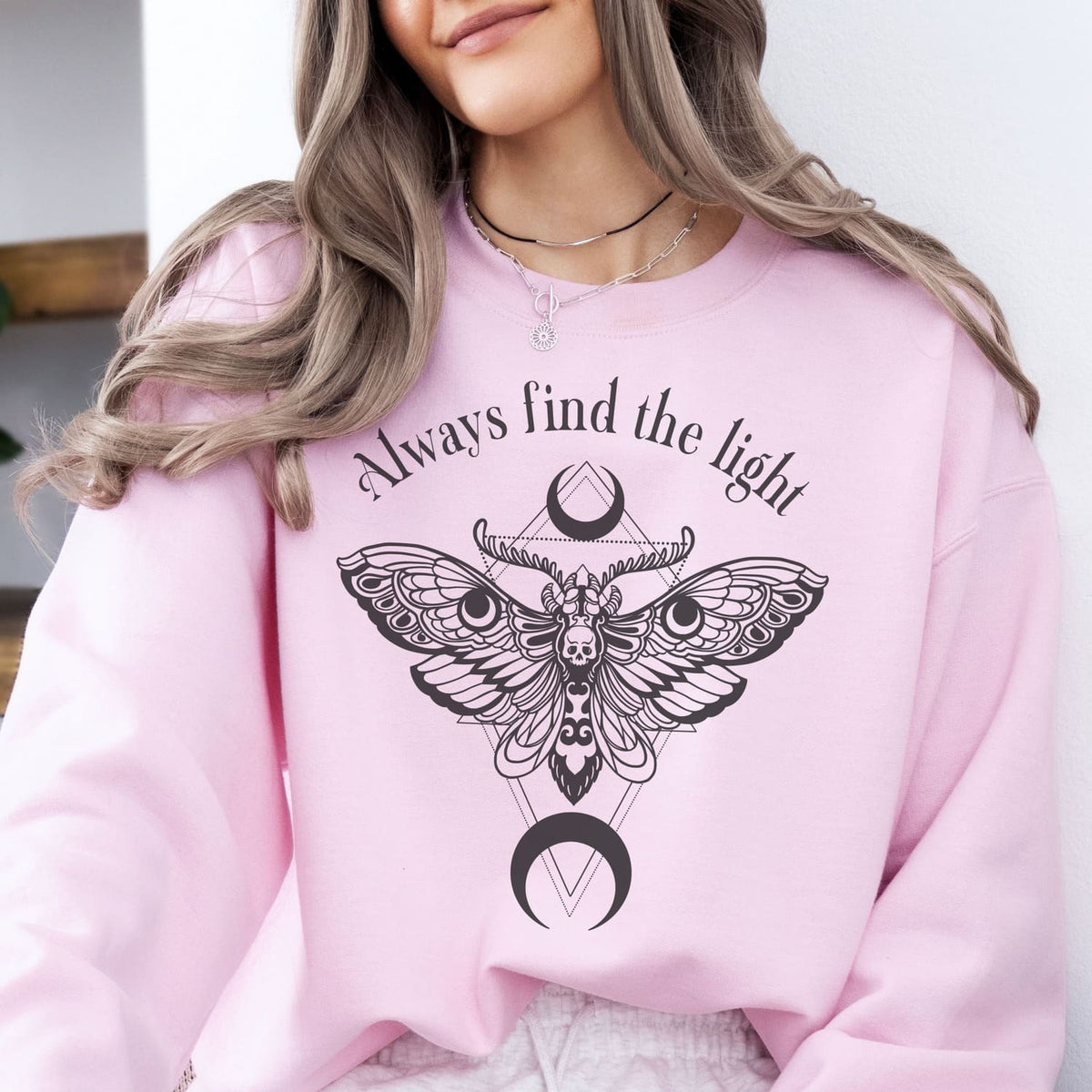 Person wearing a pink inspirational sweatshirt with a moth design and text 'Always find the light'.
