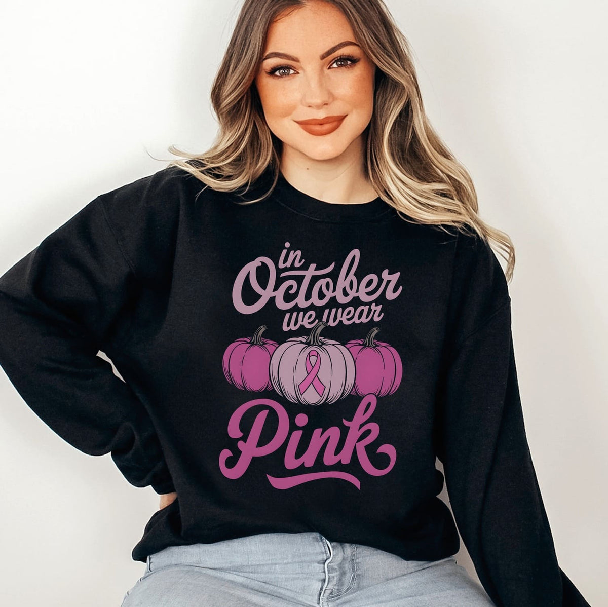 Person wearing a black sweatshirt with 'In October we wear Pink' and pumpkins breast cancer awareness pink ribbon design.