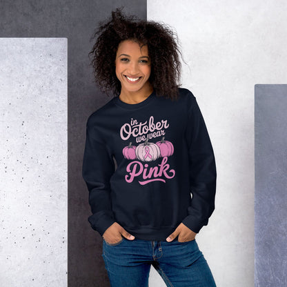 Woman wearing a navy sweatshirt with 'In October we wear Pink' text and pumpkins design breast cancer awareness pink ribbon 