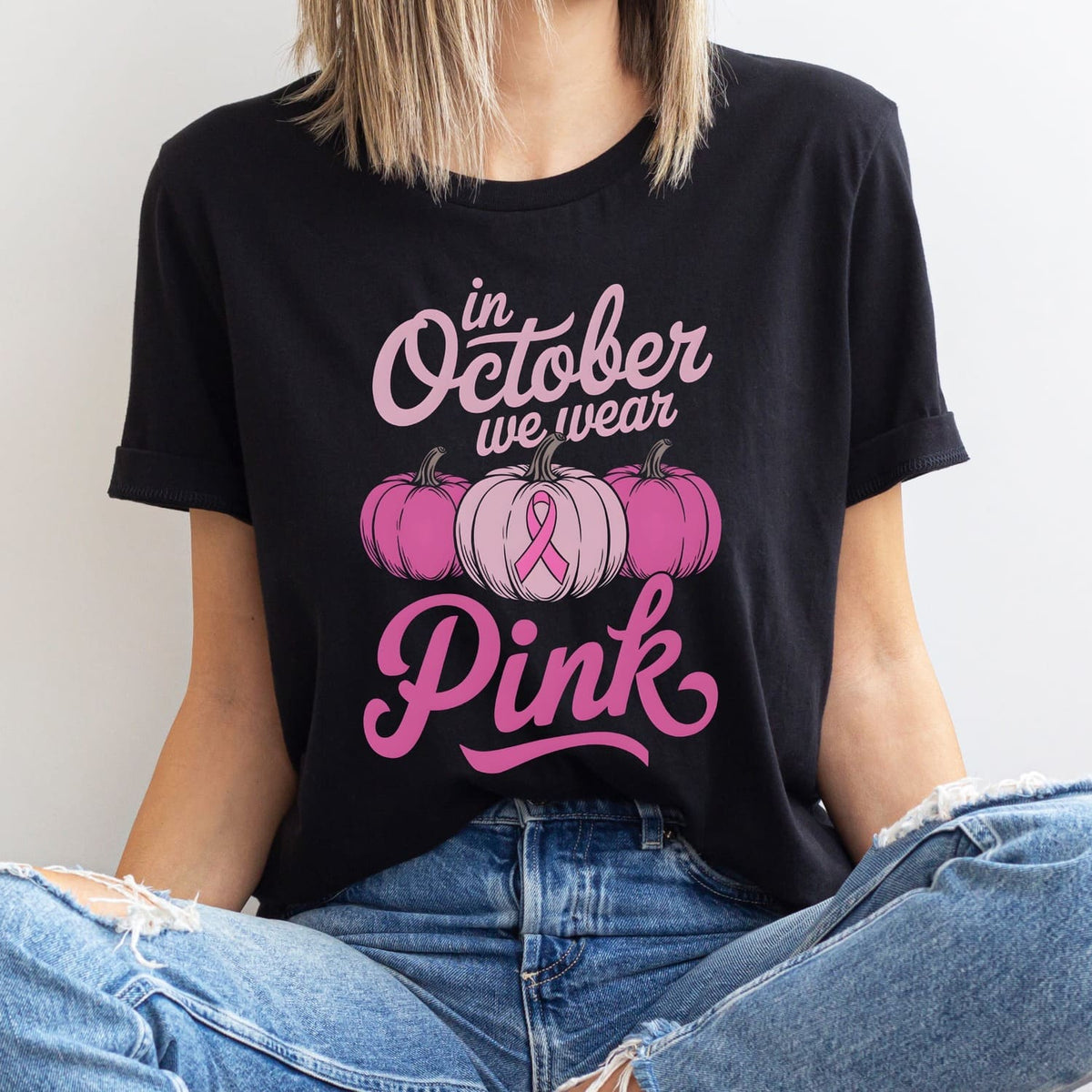 Person wearing a black breast cancer awareness t-shirt with pink ribbon and pumpkins with 'In October we wear Pink' and pumpkins design.