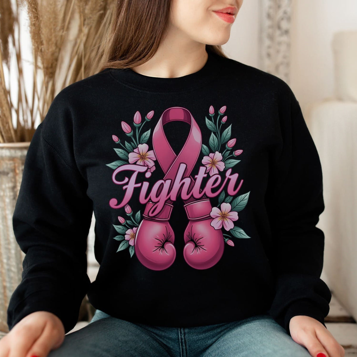 Breast cancer fighter wearing a black sweatshirt with pink boxing gloves and a ribbon design, sitting indoors.