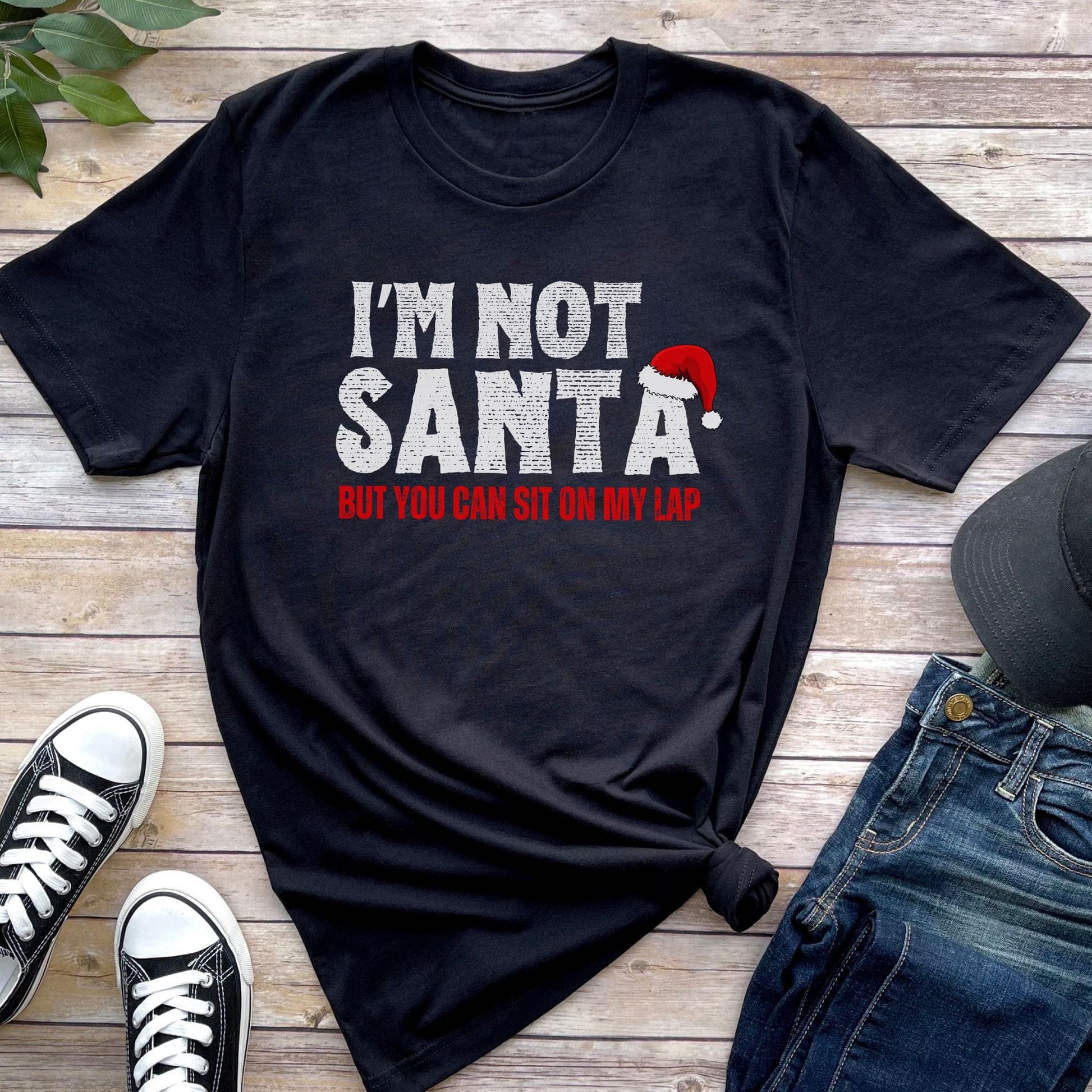 Black t-shirt with 'I'm Not Santa But You Can Sit On My Lap' text on a wooden surface with shoes and jeans: Rude Santa Men's Shirt, Adult Humor Christmas T-Shirt, Funny Holiday Season Tee For Boyfriend, Inappropriate Gift For Daddy Husband