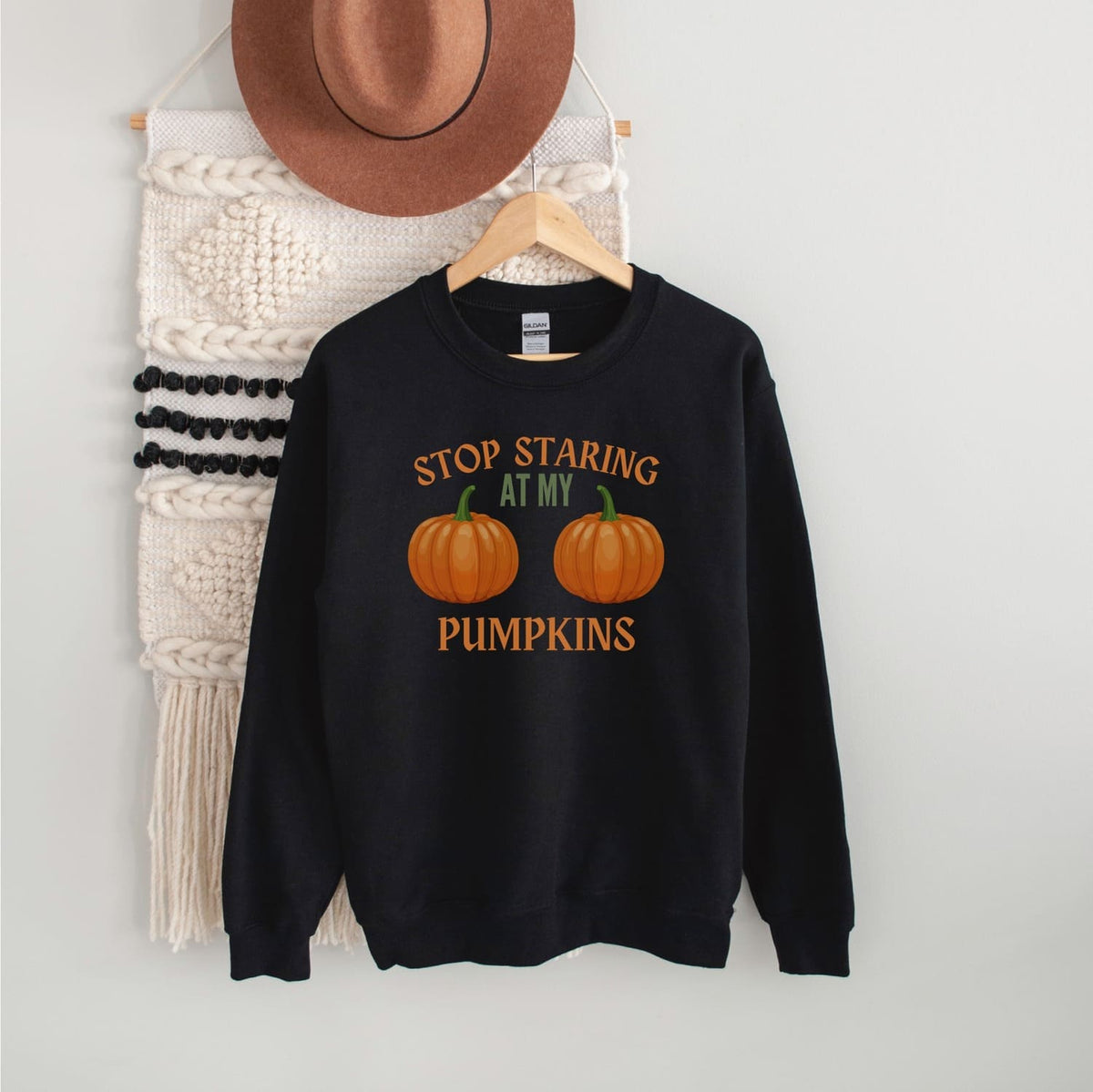 Black sweatshirt with adult humor halloween boobs on a hanger against a white wall.