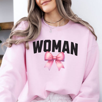 Pink mtf transgender sweatshirt with 'WOMAN' and a bow graphic, worn by a person.