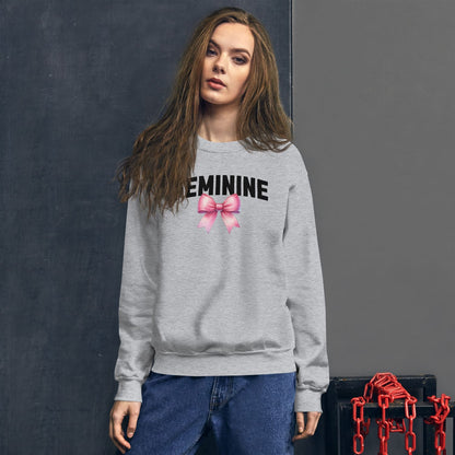 Woman wearing a gray sweatshirt with 'FEMININE' and a pink bow graphic, standing against a dark background.