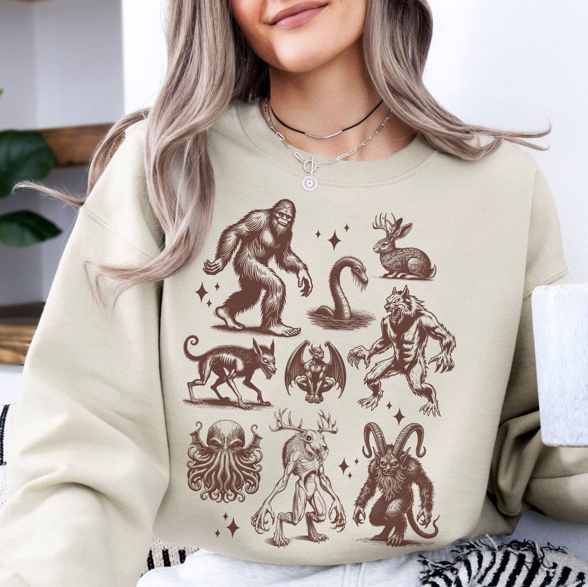 Person wearing a beige sweatshirt with cryptids creature illustrations.