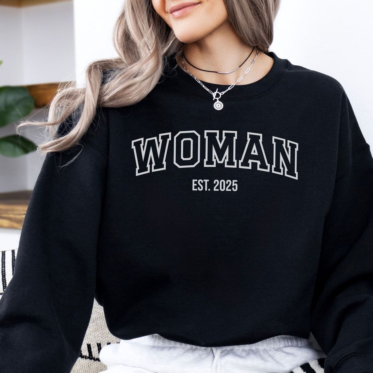 Trans MTF woman wearing a black sweatshirt with 'WOMAN EST. 2025' text.