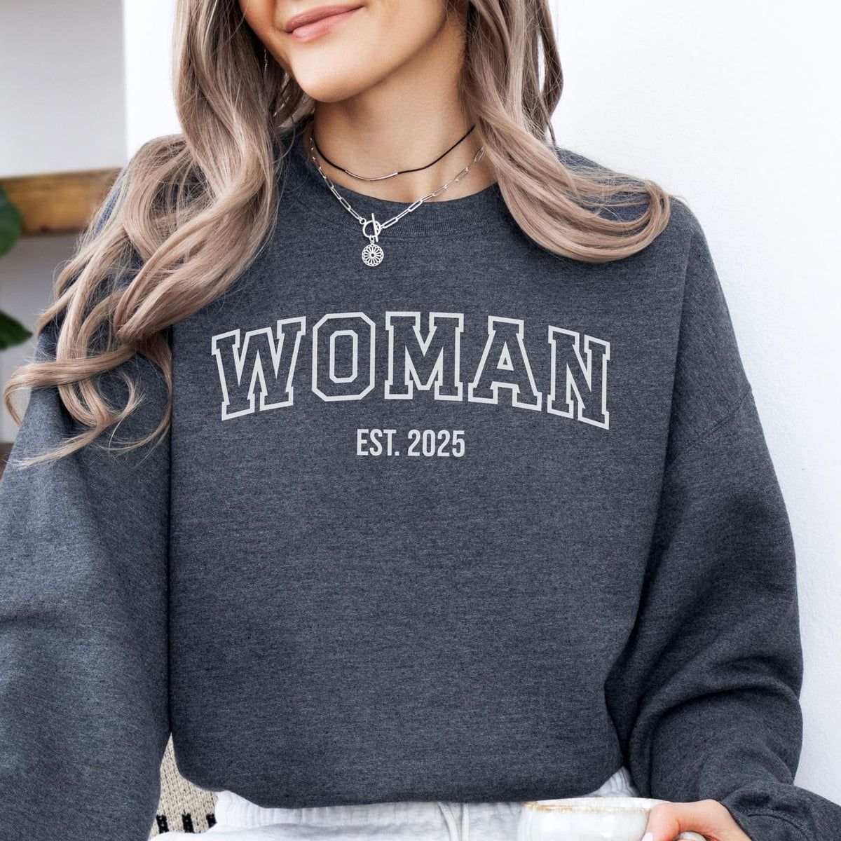 Transgender MTF  wearing a dark gray sweatshirt with 'WOMAN EST. 2025' text.