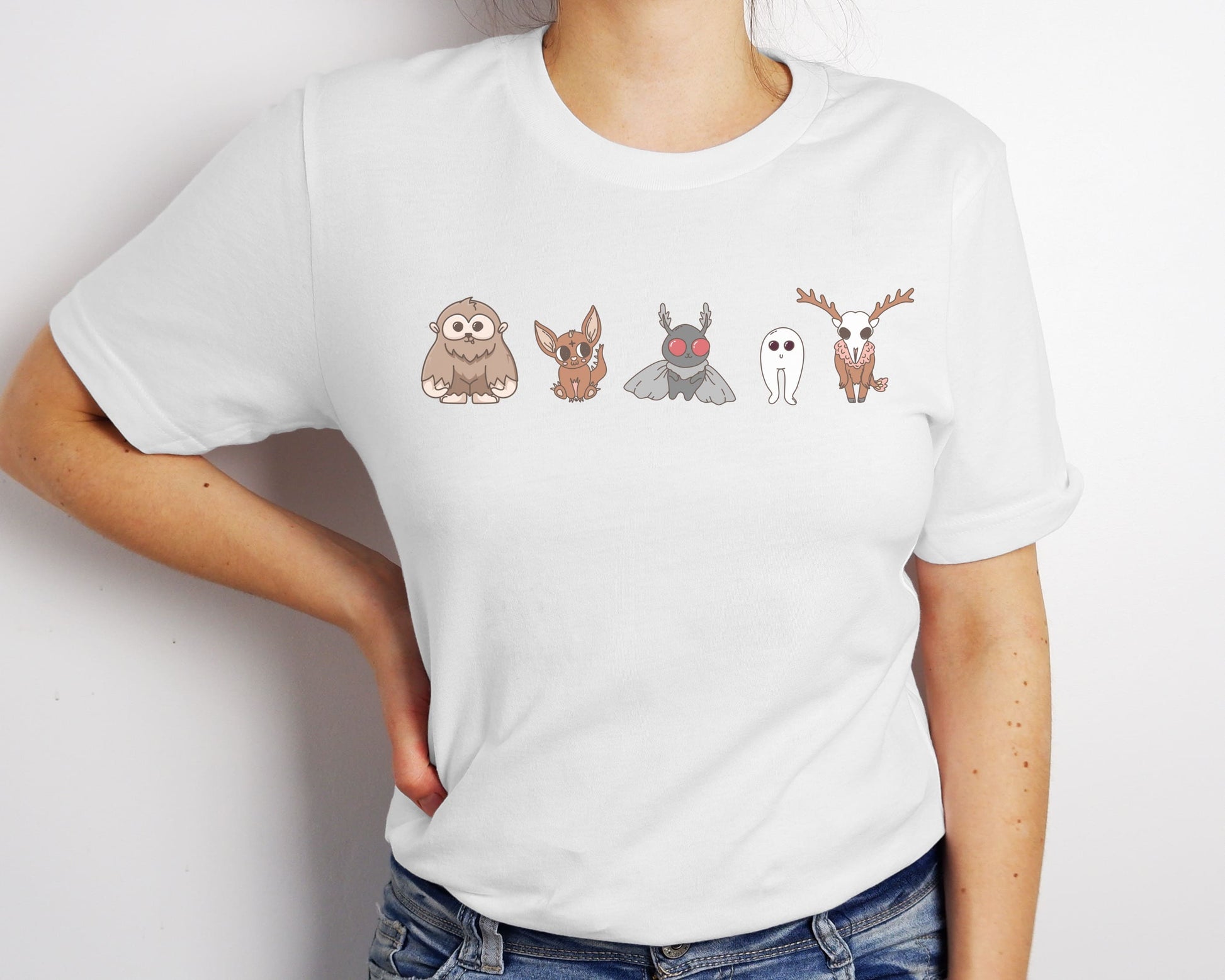 White t-shirt with cartoon character designs on a plain background: Cute Cryptids Comfort Colors Shirt, Kawaii Bigfoot Chupacabra Mothman Fresno Wendigo Tee, Funny Cryptidcore Gift, Folklore Mythology T-Shirt