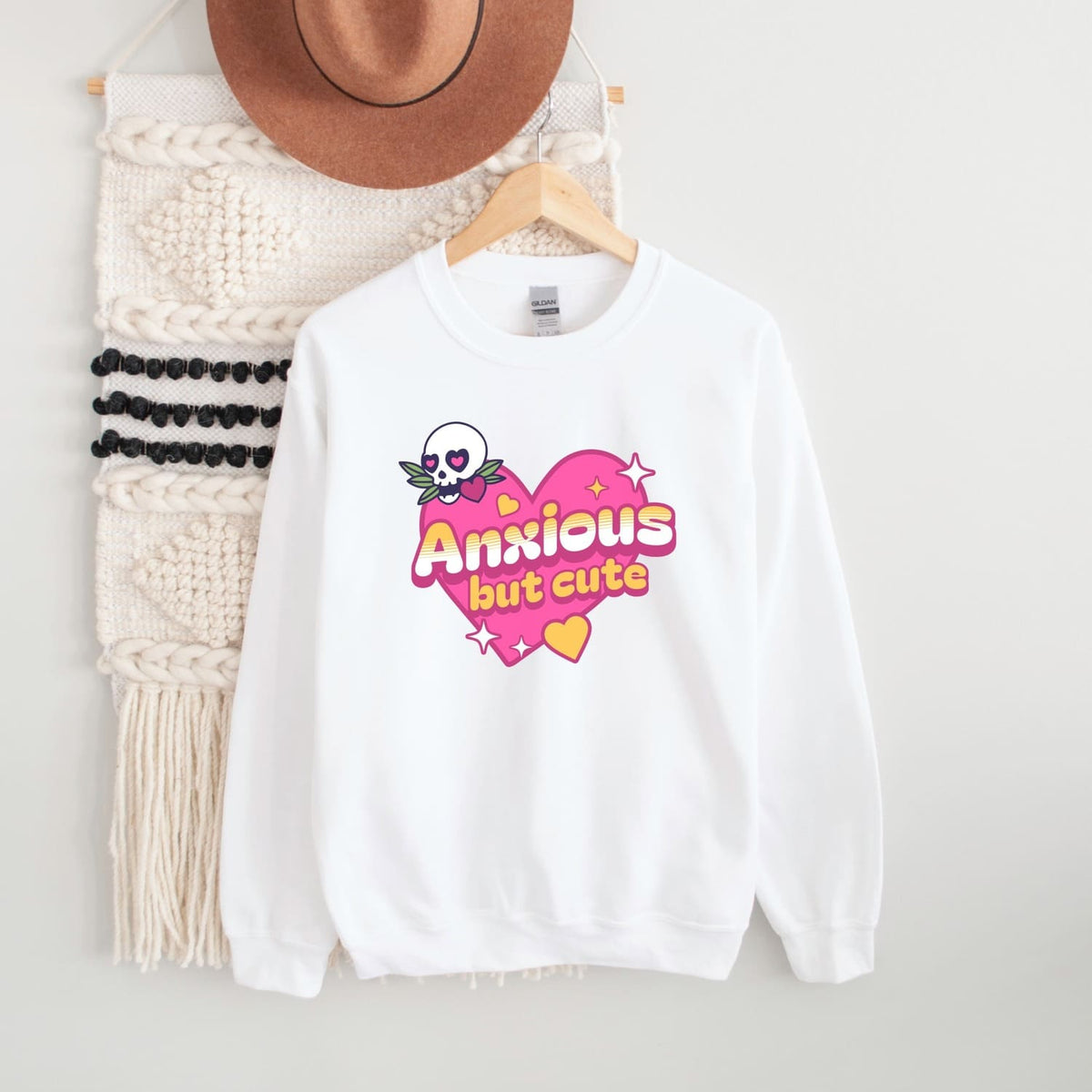 White sweatshirt with 'Anxious but cute' design on a hanger against a white background