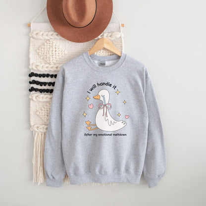 Gray mental health sweatshirt with a goose graphic and text, hanging on a wooden hanger with a hat and decorative wall piece.