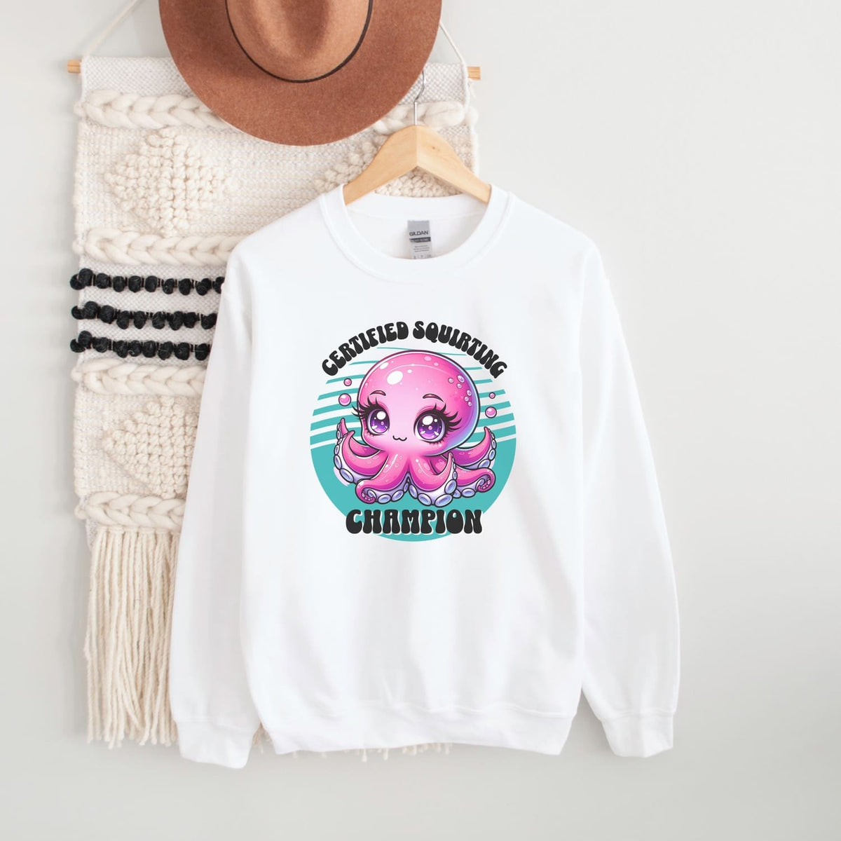 White adult humor sweatshirt with pink octopus graphic and text on a hanger with a hat and scarf in the background.