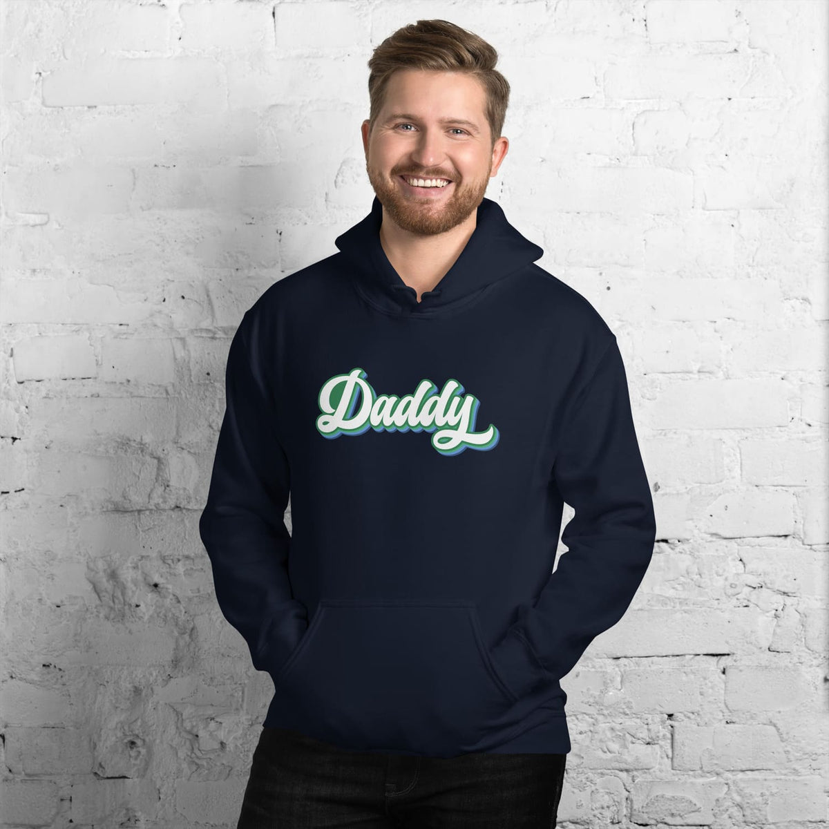 Man wearing a navy MLM gay hoodie with 'Daddy' printed on it against a white brick wall.