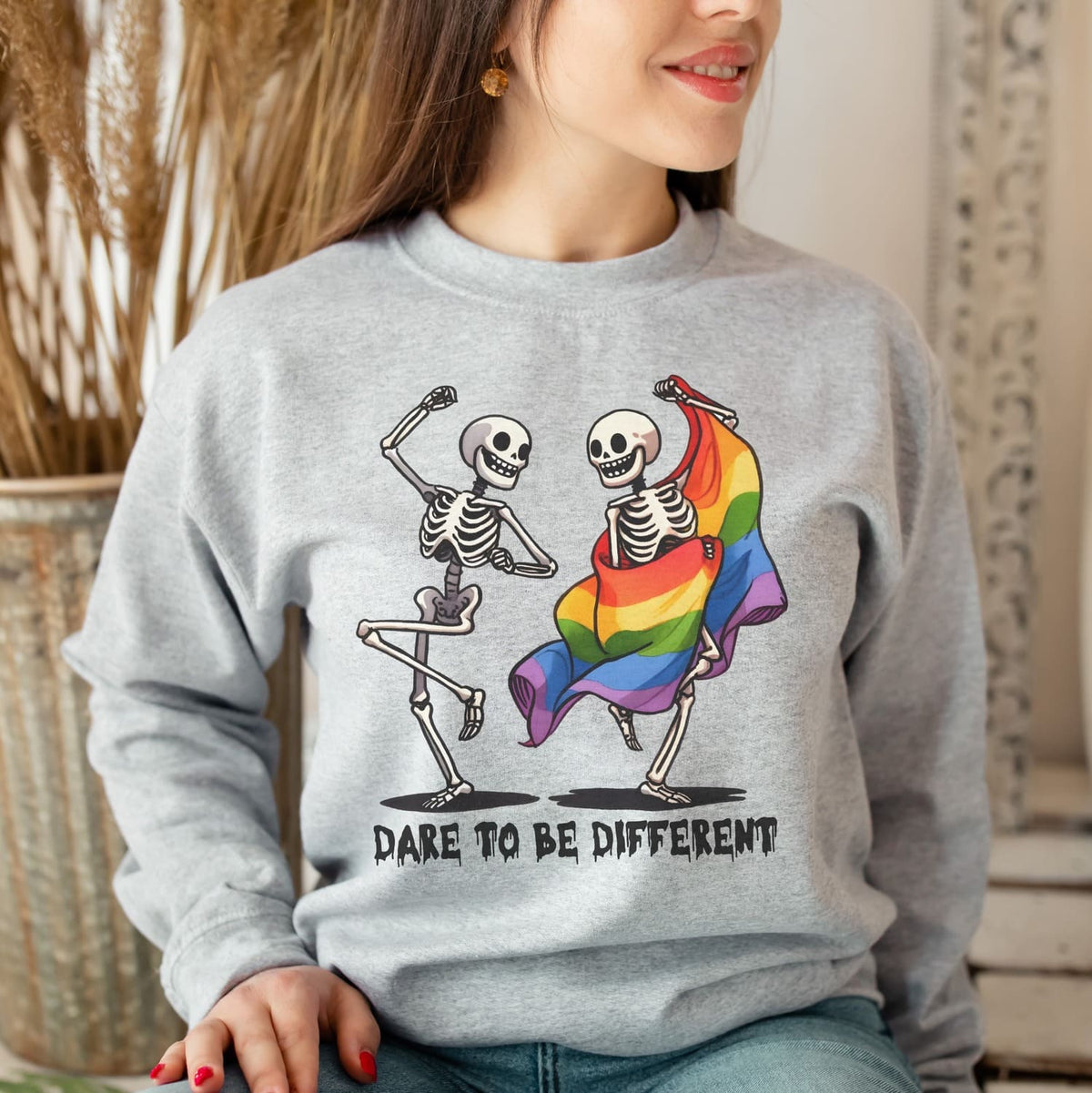 Person wearing a gray lgbt sweatshirt with skeletons dancing and a rainbow flag, with text 'Dare to be different'.