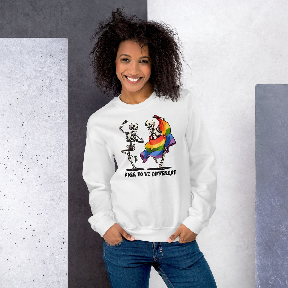Woman wearing a white lgbtq sweatshirt with a skeleton design and rainbow flag, standing against a gray and white background.