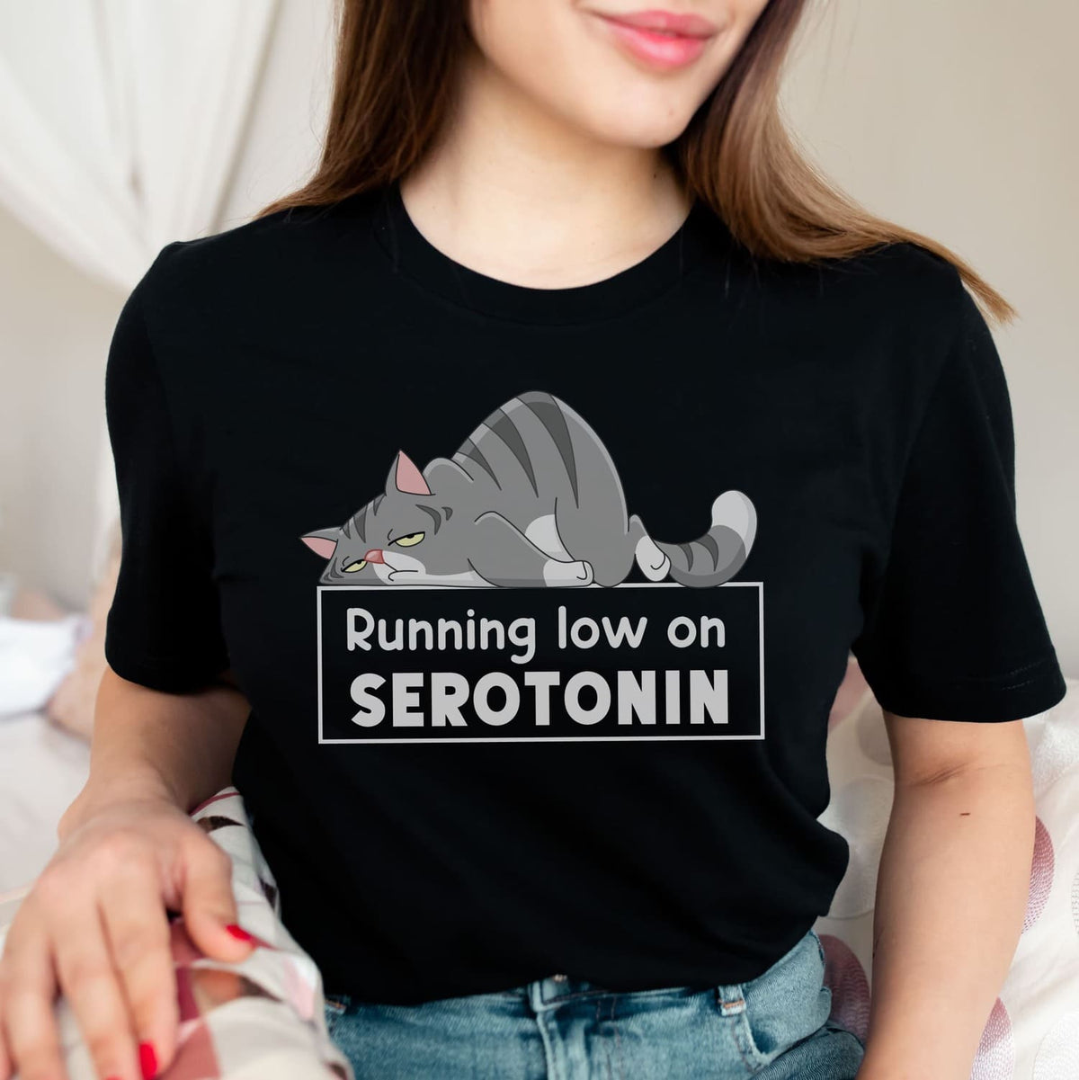 Person wearing a black mental health awareness  t-shirt with a cat graphic and text 'Running low on SEROTONIN'.