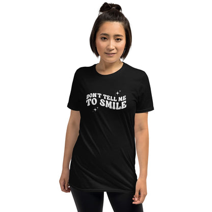Person wearing a black feminist t-shirt with 'DON'T TELL ME TO SMILE' text on a white background
